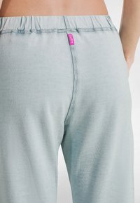 Pantalones de tela suave azul claro con una cintura elástica, que presentan una pequeña etiqueta rosa y costuras planas en la parte trasera y a los lados.