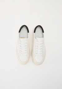 White leather sneakers with a black padded collar, white laces, and a light-colored rubber sole. Features minimal perforation design.