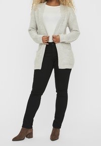 Light gray knitted cardigan with a textured pattern, open front, two pockets, long sleeves, and a relaxed fit, paired with black jeans and brown boots.