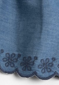 Denim fabric in blue with scalloped edge. Features navy blue floral embroidery along the bottom. Textured surface, smooth finish.