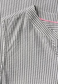 Chemise à rayures présentant des rayures noires et blanches alternées, avec un col rond et une couture d'accent rose au niveau du col. Texture douce.