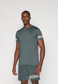 Dark green athletic t-shirt with short sleeves, round neckline, and white "BORG" logo on the left sleeve. Soft, smooth fabric; paired with matching shorts.