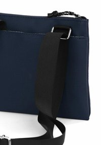 Tmavě modrá kabelka přes rameno z texturované látky, s černým nastavitelným popruhem a stříbrným kovovým zapínáním na zip.