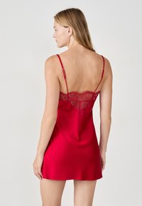 Abito sottoveste in raso rosso con pizzo lungo il retro e spalline sottili e regolabili. Texture liscia, lunghezza corta e design elegante.