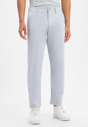 Man draagt lichtgrijze rechtvallende broek met knoop en rits, gecombineerd met witte sneakers op een witte achtergrond.
