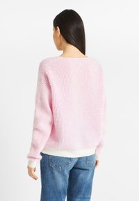 Różowy sweter dzianinowy w paski o luźnym kroju, z długimi rękawami i szerokim ściągaczem. Miękka struktura i kontrastowy biały dolny pas.