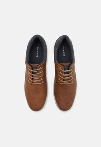 Chaussures décontractées synthétiques marron avec une texture lisse, bout rond et lacets beiges. Doublées d'un tissu bleu foncé avec un col gris.