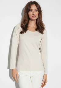Jasnobeżowa bluzka z długim rękawem o okrągłym dekolcie, wykonana z gładkiego materiału, dopasowany fason i minimalne detale przeszycia.