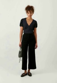 Σκούρο μπλε τοπ με φουσκωτά μανίκια και βαθύ V-ντεκολτέ, συνδυασμένο με μαύρα παντελόνια με ψηλή μέση και φαρδιά γραμμή, και μια μικρή πλεκτή τσάντα. Μαύρες επίπεδες παπούτσια.