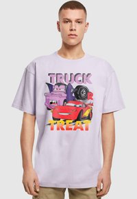 Laventelivärinen puuvillapaita, jossa on värikäs graafinen kuvasto autoista ja teksti "TRUCK OR TREAT". Irtonainen malli, lyhyet hihat, pyöreä kaula-aukko.