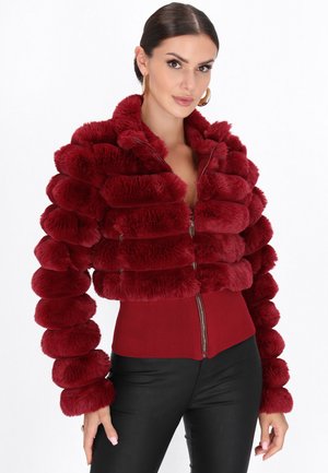 Rode nep bont gecropte jas met ronde pompontextuur, ritssluiting en lange mouwen, gecombineerd met een fitted rode top en zwarte broek.