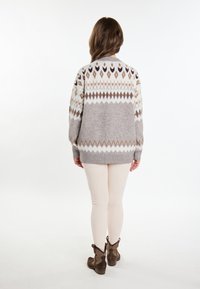 Maglione grigio con un motivo geometrico in beige chiaro, marrone e viola scuro. Tessuto morbido. Abbinato a leggins pallidi e stivali alla caviglia marroni.