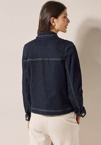 Veste en denim noir avec un col classique, des coutures sur le panneau avant et des poignets boutonnés. Détails de coutures visibles et design ajusté.