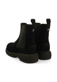 Botines de ante negro con paneles laterales elásticos, suelas de goma gruesa y texturizada, y tiradores en la parte trasera para facilitar su uso. Logo de la marca en el tacón.