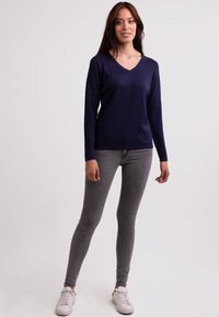 Námořnický svetr s V-výstřihem vyrobený z měkkého materiálu, doplněný o šedé slim-fit džíny a bílé tenisky; ležérní design s dlouhými rukávy.