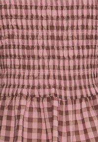 Detailní záběr na růžovou a hnědou kostkovanou látku se sbíranými, nařasenými sekcemi, které vytvářejí strukturu a vodorovné linie.