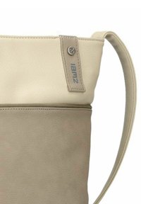 Beigefarbene Ledertasche mit glatter Textur, versehen mit einem kontrastierenden hellbraunen unteren Abschnitt, einem Schultergurt und einem Markenakzent nahe dem oberen Rand.