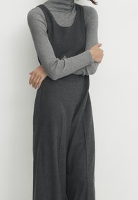 Grijze wollenblend jumpsuit met wijde benen en een aansluitende bodice, gelaagd over een lichtgrijze ribgebreide coltrui. Soepele textuur, minimalistisch ontwerp.