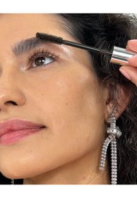 Svart mascara blir påført med en spoolie-børste. Synlige vipper og lys hudtone. Pendeløreringer med klare diamantlignende akenter.