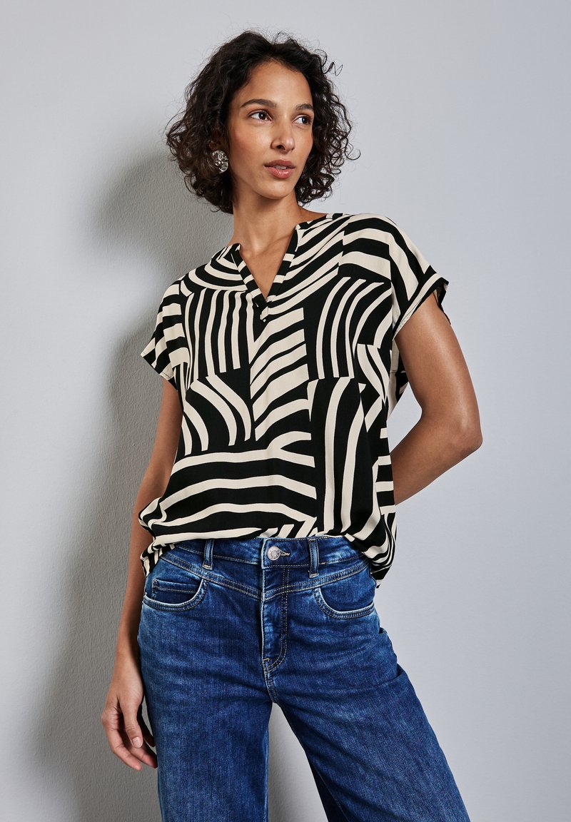 Blusa a fantasia nera e crema con scollatura a V e maniche corte, abbinata a jeans in denim blu con un classico design a cinque tasche.