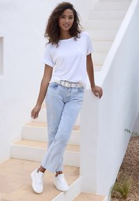 LÄSSIGES WEISSES T-SHIRT, HELLBLAUE JEANS, WEISSE TURNSCHUHE. AKZENT MIT METALLISCHEM GÜRTEL, RUNDEN TREPPENHAUS-HINTERGRUND, NATÜRLICHE TEXTURELEMENTE.