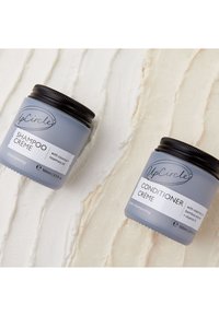 Szare słoiki z etykietami "Szampon Krem" i "Odżywka Krem" z czarnymi pokrywkami, oba o pojemności 100 ml, umieszczone na teksturowanym kremowym tle.