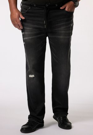 Pantalones de mezclilla negra con un corte relajado, que presentan áreas desgastadas y detalles desgastados. Combinados con zapatos negros con cordones.