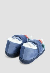 Blå plyschbarnslipper med vit fluffig foder och flerfärgade mjuka former på toppen, visade mot en enkel bakgrund.