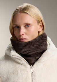 Brun ribbet strik turtleneck lagd over en creme, faux fur zip-up jakke. Glat tekstur med en høj krave, ingen synlige mønstre eller detaljer.