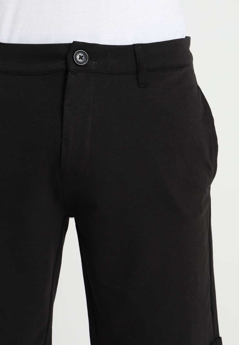 Pantalones negros con cierre de botones en la parte delantera, dos bolsillos laterales y una textura suave. La tela parece ligera y versátil para el uso casual.