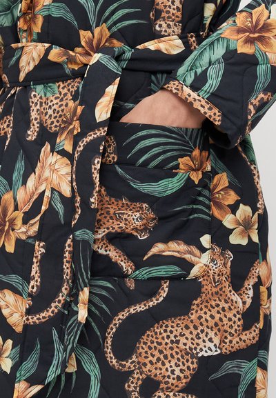Kurtka z pikowanej tkaniny z czarnym tłem, zdobiona intensywnymi wzorami kwiatowymi i w leopardzie, wyposażona w pas z klamrą i detalami w postaci kieszeni bocznych.
