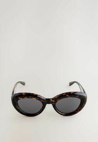 Gafas de sol de carey con lentes ovalados de gran tamaño. Patrón suave en negro y marrón, marco elegante y brazos curvados. Lentes oscurecidos.