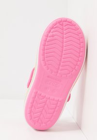 Vaaleanpunainen kuminen kenkäpohja, jossa on teksturoitu, sahalaitamainen pinta; siinä on sileä reuna ja painettu logo; hieman kohotettu, jossa on tukeva pito.