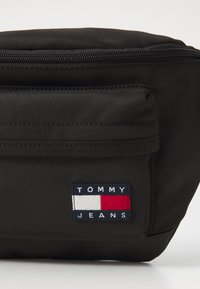 Schwarze Nylon-Tasche mit vorderer Reißverschlusstasche und Tommy Jeans-Logopatch mit einem rechteckigen Design in Weiß, Rot und Marineblau.