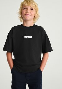 Sort bomulds-T-shirt med en hvid "FORTNITE"-logo centralt placeret på fronten. Korte ærmer med en afslappet pasform og rund halsudskæring.