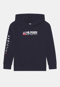 Felpa con cappuccio blu navy con logo frontale e testo bianco sulle maniche. Realizzata in tessuto morbido con polsini e orlo a costine.