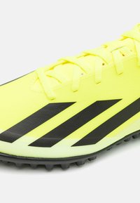 Scarpa da ginnastica gialla brillante con strisce nere, tomaia testurizzata e suola a contrasto. Presenta chiusura con lacci e suola chiodata per una migliore aderenza.