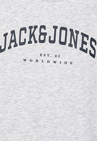 Szary materiał z czarnym napisem "JACK&JONES" w łuku nad mniejszym napisem "EST. 90 WORLDWIDE" nadrukowanym na powierzchni.