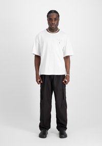 Camiseta blanca oversize con estampado de "BERLÍN", combinada con pantalones cargo negros y zapatillas negras sin cordones. Diseño simple, ajuste casual, textura suave.