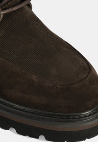 Bruine suède boot met een corduroy bovenwerk, dikke zwarte rubberen zool en een gestructureerde afwerking. Subtiele contraststeek langs de rand.