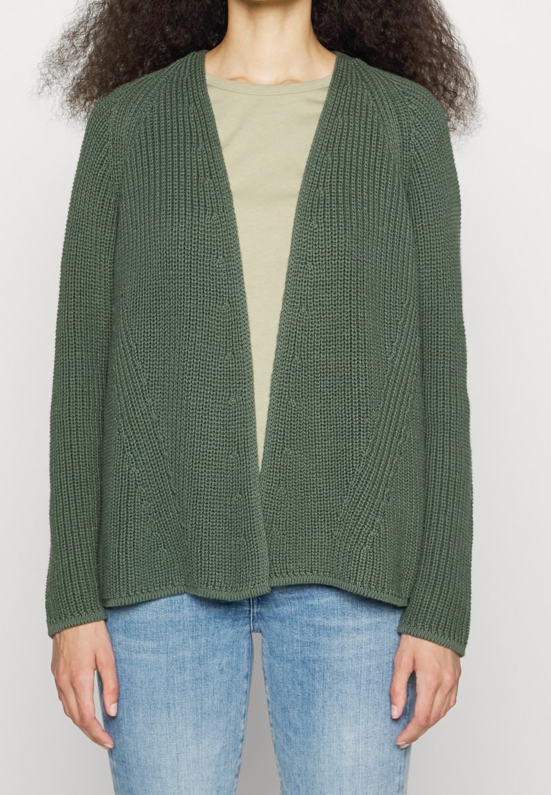 Knit cardigan in dark green, open front, textured fabric with vertical ribbing and a loose fit. Paired with a light green shirt and jeans.