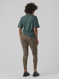 Grünes Baumwoll-T-Shirt mit kurzen Ärmeln, kombiniert mit Leggings im Leopardenmuster in Brauntönen und Schwarz sowie schwarzen Schnürschuhen.