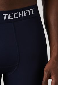 Marineblauwe sportlegging met een TECHFIT-logo op een contrasterende tailleband. De stof is soepel met zichtbare stikdetails.