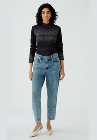 Dunkel lila und grau gestreiftes langärmliges Oberteil mit hohem Kragen, kombiniert mit hellblauen, hoch taillierten, geraden Jeans und beigen spitz zulaufenden Schuhen.