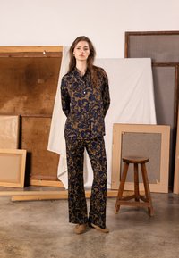 Sada košile a kalhot v námořnické modré a zlaté barvě s květinovým vzorem, obsahující košili s límečkem a široké kalhoty, doplněná neutrální obuví.