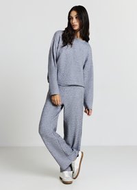 Sportliches graues Strick-Sweatshirt und passende weite Hose mit entspanntem Schnitt und gerippten Bündchen, kombiniert mit weißen Sneakers.