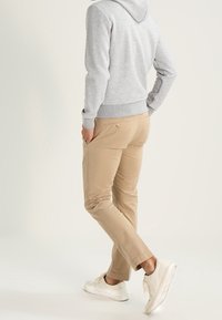 Grå hoodie med en framficka, ihop med beige chinos. Chinosen har slim-fit och bakfickor. Vita sneakers fulländar looken.