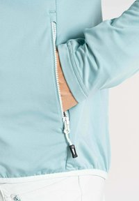 Hellblaues Jacket mit einer Reißverschlusstasche. Glatter Stoff, taillierte Passform, elastische Bündchen und ein Reißverschlussanhänger mit einem kontrastierenden schwarzen Akzent.