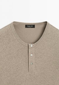 T-shirt Henley beige avec col rond et trois boutons sur la patte de boutonnage, avec l'étiquette de la marque Massimo Dutti visible à l'intérieur du col.