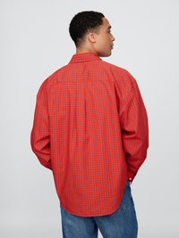 Röd knäppskjorta med ett geometriskt blått mönster, långa ärmar och en ryggdetalj. Kombinerad med denimbyxor.